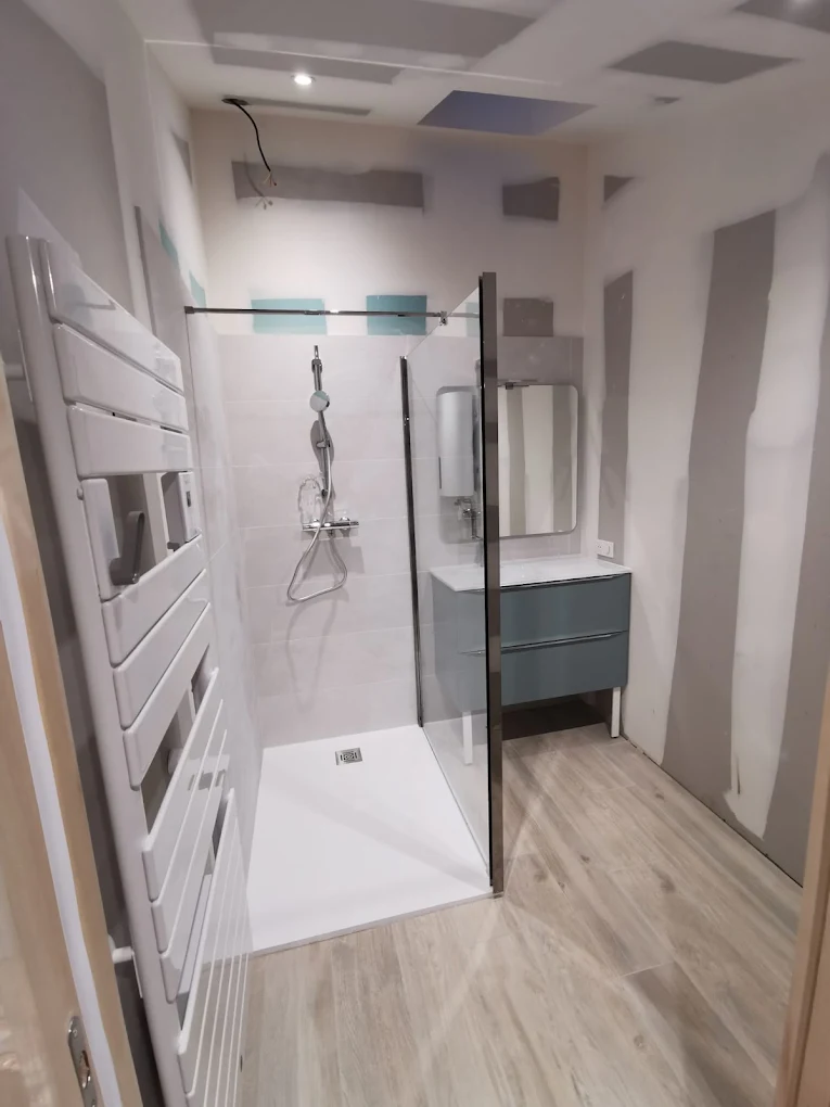 Douche avec receveur extra-plat, paroi vitrée, sèche-serviettes et meuble vasque dans une salle de bain neuve