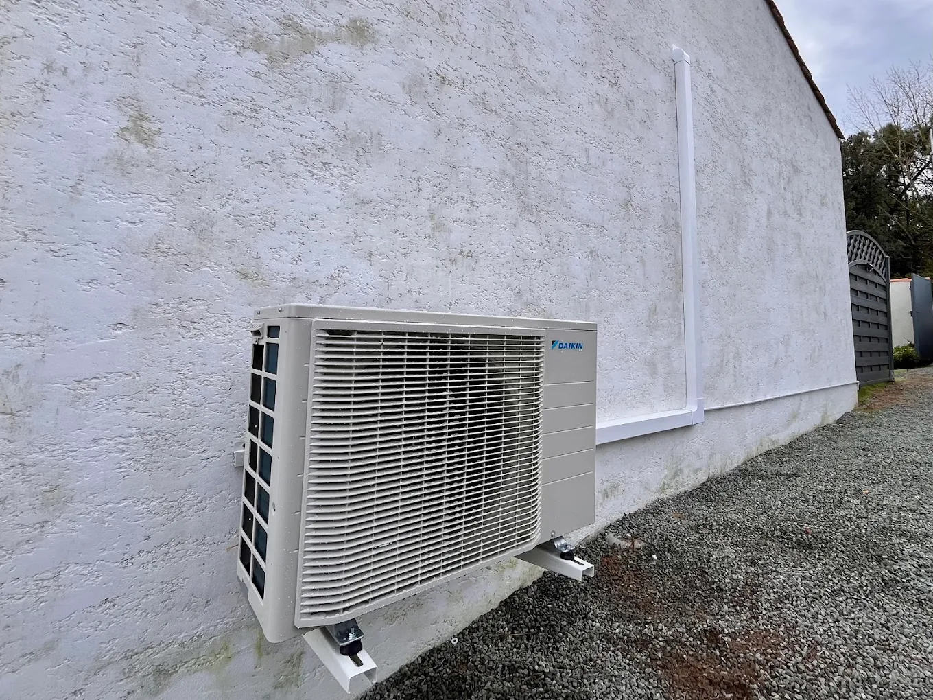 Unité extérieure Daikin fixée sur consoles murales avec goulotte blanche le long du pignon