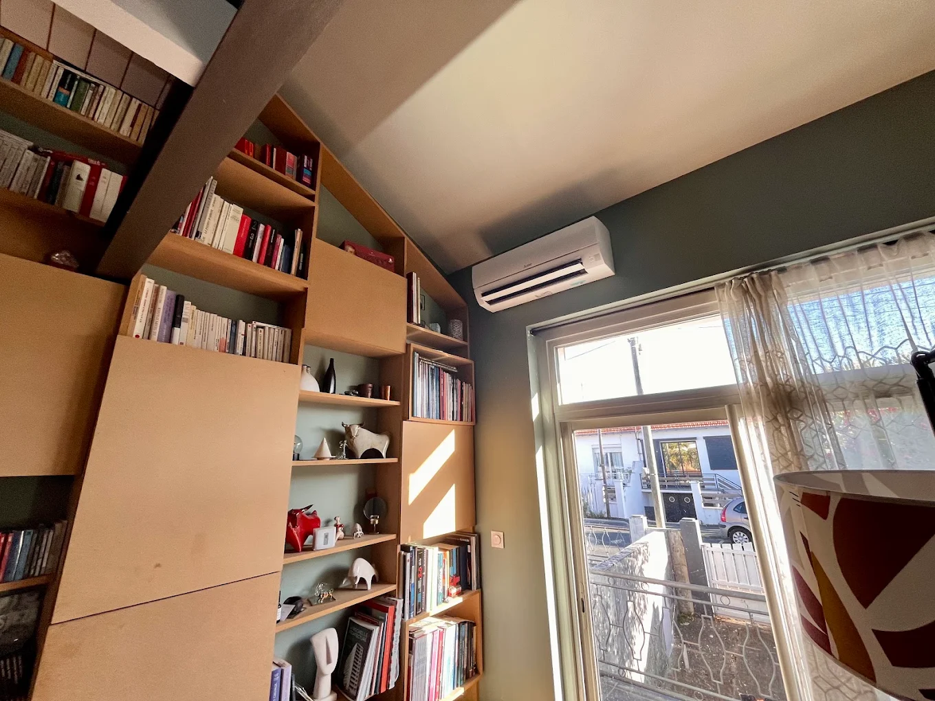 Split mural de climatisation réversible installé dans un salon-bibliothèque près d'une porte-fenêtre