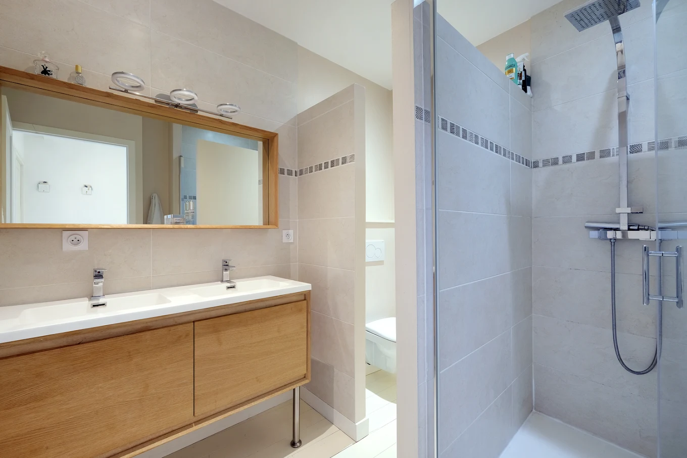 Salle de bain avec double vasque sur meuble bois, miroir et douche à porte vitrée